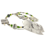 A gray, black, white, yellow, and green beaded necklace with a large, tower-shaped stone pendant lies on a white background.
