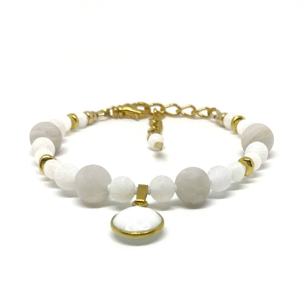 A bracelet with white and pale-gray beads, gold-toned accents, and a white and gold-toned charm lies on a white background. 