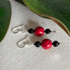 A pair of silver-toned earrings with red and black beads lies on an ivory fabric background with green leaves to the top and sides. The black beads are fluted, and the red ones have a design carved into them.