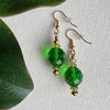 Green beaded earrings on an ivory background with green leaves.