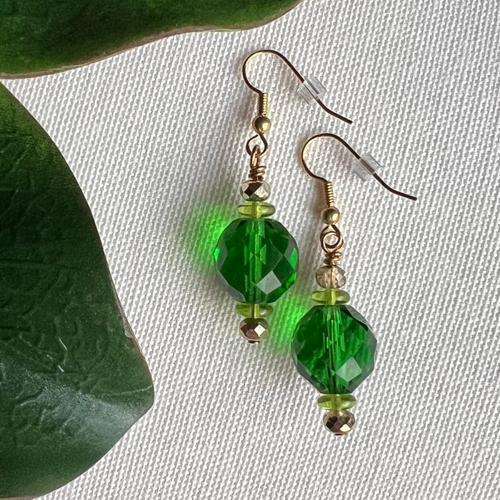 Green beaded earrings on an ivory background with green leaves.