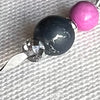 The photo is a close-up of a pointed silver headpin holding silver, silver-crackled gray, and orchid-pink beads.