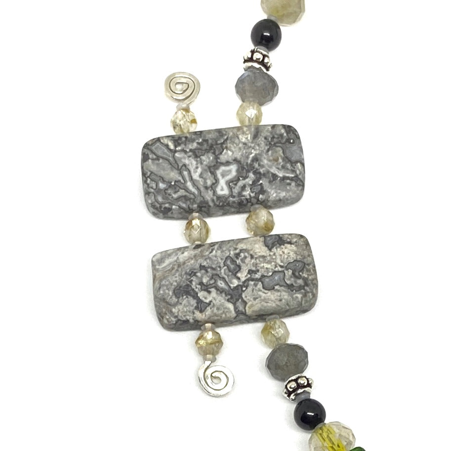 A strand of black, silver, gray, and yellow beads lies on a white background. Two of the gray beads are double-drilled and feature silver wire with spirals at the ends.