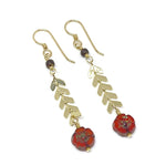 On a white background lies a pair of earrings with gold-toned metal components. Each features a small brown wood bead, below which is a short length of chevron chain, finished with a scarlet flower-shaped bead.