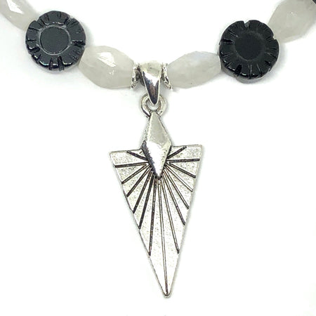 A line of black and white beads curves across the top part of the photo, and at the center is a silver-toned pendant featuring a pattern of sun rays. The background is white.