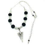Black, white, and silver-toned "Starlit Garden" necklace, from the STARSNOW Collection, lies on a white background with the chain curved to one side. The necklace features black and white beads and a silver-plated arrowhead-shaped pendant decorated with lines that resemble the sun's rays.