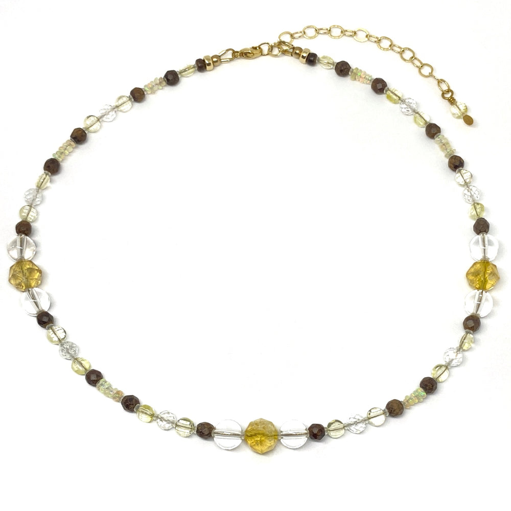 A necklace with clear, yellow, and brown beads lies on a white background with the golden extender chain curved toward the upper right corner.